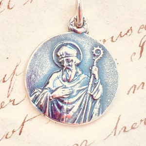 Peut inclure: Pendentif en argent représentant une image détaillée de Saint Patrick tenant une crosse. Le pendentif est circulaire et a une finition texturée.