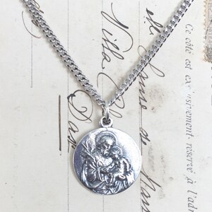 May include: Silver chain necklace with a round pendant featuring a detailed image of Saint Anthony of Padua holding a baby Jesus.