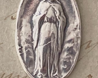 May include: Silver oval-shaped pendant featuring a detailed image of the Virgin Mary with a crown, standing with hands clasped in prayer. The pendant has two rings on either side for attaching to a chain.