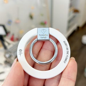 May include: White keychain with a silver ring and the text "GLORY IN THE FLOWER" and "SAHARA SAND" engraved on it.