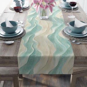 May include: A teal and beige table runner with a wavy pattern reminiscent of ocean waves. The runner is laid on a wooden table with place settings on either side.