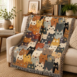 May include: A woven throw blanket featuring a repeating pattern of stylized cats in various colors including orange, gray, black, and white. The blanket has a textured surface with visible thread details and a fringed edge along the sides.