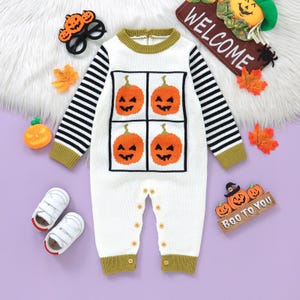May include: A white baby's Halloween-themed romper with four orange pumpkin faces on the front. The sleeves have black and white stripes. The romper is surrounded by Halloween decorations, including a welcome sign and baby shoes.