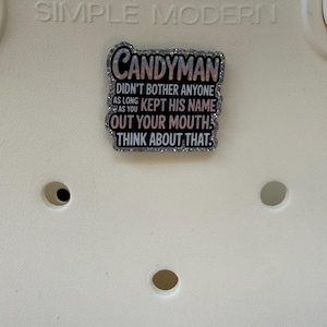 K&ouml;nnte beinhalten: Dekorative Anstecknadel mit dem Wort "CANDYMAN" und dem Zitat "DIDN'T BOTHER ANYONE AS LONG AS YOU KEPT HIS NAME OUT YOUR MOUTH. THINK ABOUT THAT." Die Anstecknadel hat einen glitzernden Rand und ist vor wei&szlig;em Hintergrund.