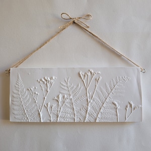 Könnte beinhalten: Weißer rechteckiger Wandbehang mit einem erhabenen Design aus Farnen und Wildblumen. Der Wandbehang hat ein rustikales Bindfadenband zum Aufhängen.