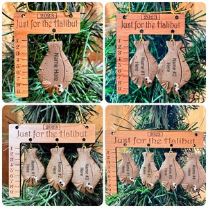May include: Wooden Christmas ornaments with the text "Just for the Halibut" and the year 2023. Each ornament features a fish-shaped design with a ruler and space for a name. The ornaments are brown and hang from gold strings.