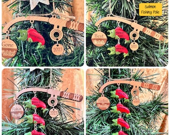 May include: Wooden fishing pole Christmas ornaments with red fish, green fish, and the text "Gone Fishin'", "Best Catch", "Fishin Family", and "Hooked Family". Each ornament includes the year 2023.
