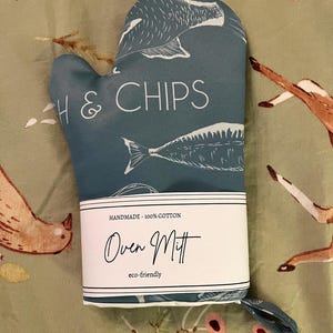 May include: A teal oven mitt with a fish and chips design. The mitt is made of 100% cotton and features the words "H & CHIPS" and "Oven Mitt". The mitt is eco-friendly and has a loop for hanging.