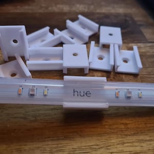 May include: White plastic clips for mounting a Philips Hue light strip. The strip is labeled "hue" and has three LEDs.