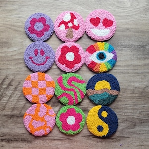 May include: Twelve colorful round embroidery hoops with various designs, including a flower, a mushroom, a smiley face, an eye, a checkered pattern, a swirl pattern, a sunset, and a yin yang symbol.
