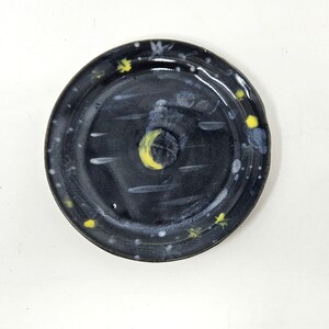 May include: A black ceramic plate with a white and yellow moon and stars design.