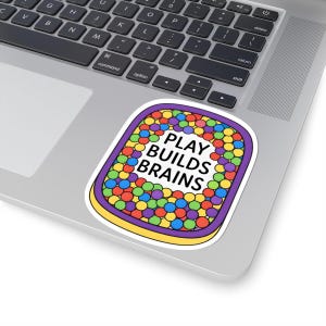 May include: A colorful sticker with the text "PLAY BUILDS BRAINS" inside a purple and yellow border. The sticker is filled with small, round, multi-colored shapes.