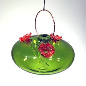 May include: A green glass hummingbird feeder with a wire hanger and three red glass flowers.