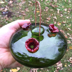 May include: A green glass hummingbird feeder with three red glass flower feeding ports and a copper wire hanger.