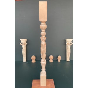 May include: A wooden decorative column with a carved female figure and ornate details. The column is on a wooden base and there are three smaller wooden finials on either side.