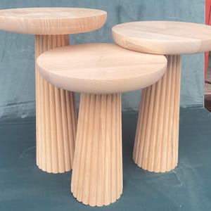 May include: Three wooden nesting tables with fluted legs. The tables are made of light wood and have a natural finish.