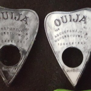 May include: Two white Ouija planchette boards with black lettering. The boards have the letters of the alphabet, numbers 1-9 and 0, and the words "yes", "no", and "goodbye".