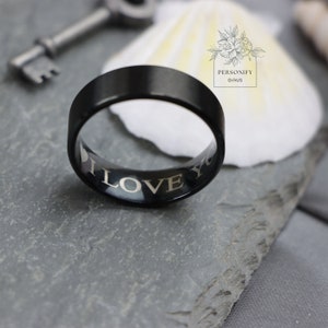 May include: A black ring with a beveled edge and the words "I LOVE YOU" engraved on the inside.