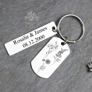 May include: A silver keychain with two tags. One tag has the text "Rosalie & James 08.12.2000" and the other tag has a floral design.