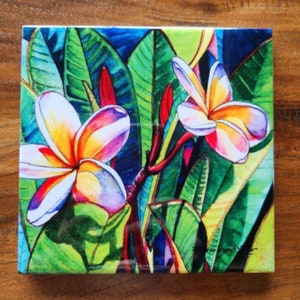 May include: A colorful ceramic tile with a painting of white plumeria flowers with yellow centers and pink edges. The flowers are surrounded by green leaves with red stems.