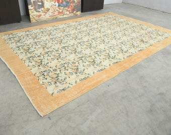 May include: A rectangular area rug with a floral pattern in cream, peach, and green. The rug has a peach-colored border. The rug is placed on a gray concrete floor. The rug is a decorative floor covering.