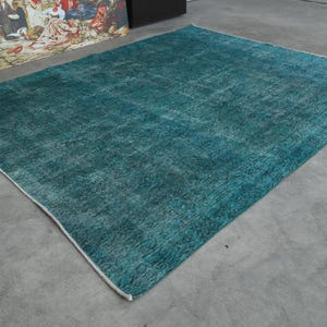 May include: A teal blue rug with a distressed, vintage look. The rug has a white border and is made of a soft, woven material.