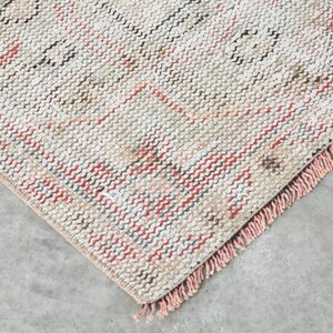 May include: Close-up of a woven rug with a fringed border. The rug has a cream background with pink, red, and blue stripes.