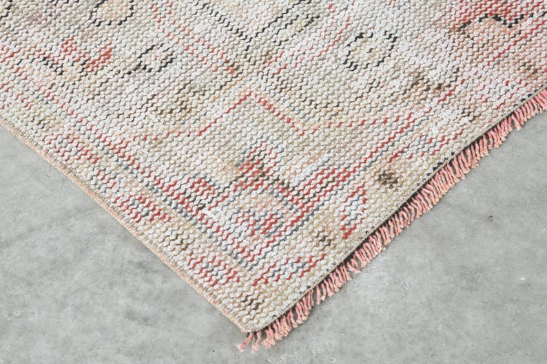 May include: Close-up of a woven rug with a fringed border. The rug has a cream background with pink, red, and blue stripes.