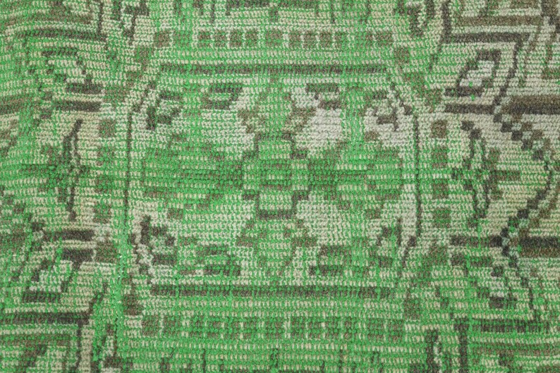 May include: A woven textile featuring a repeating geometric pattern in vibrant green and muted beige tones. The design consists of intricate interlocking shapes, lines, and symmetrical motifs that create a textured, grid-like appearance across the surface.