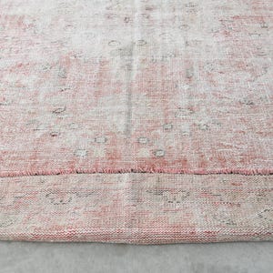 May include: A vintage pink and white rug with a faded floral pattern. The rug has a frayed edge and is made of a soft, woven material.