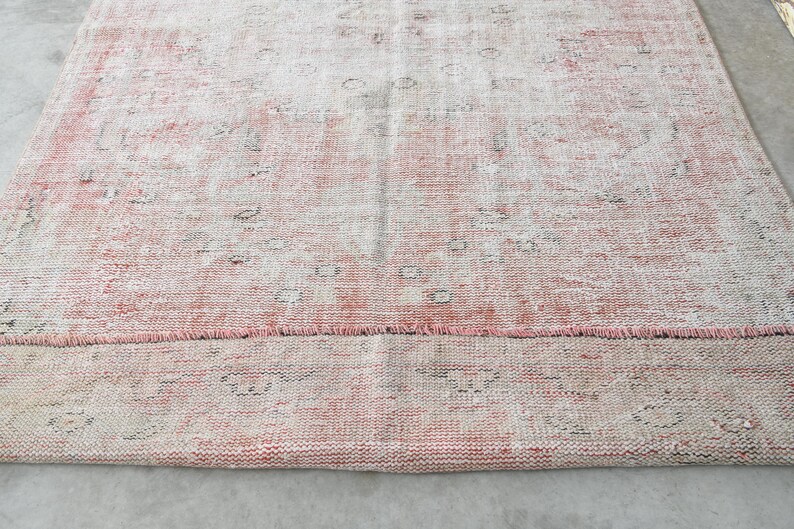 May include: A vintage pink and white rug with a faded floral pattern. The rug has a frayed edge and is made of a soft, woven material.