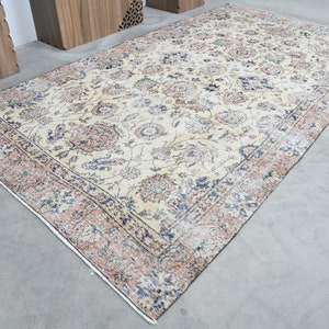 May include: A vintage rug with a cream background and a floral pattern in shades of blue, pink, and brown. The rug has a border with a repeating pattern.