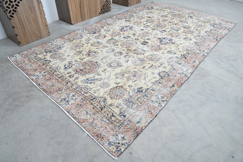 May include: A vintage rug with a cream background and a floral pattern in shades of blue, pink, and brown. The rug has a border with a repeating pattern.