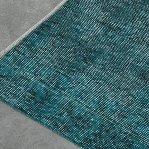 May include: Close-up of a teal blue rug with a woven texture. The rug has a distressed look with a faded pattern.