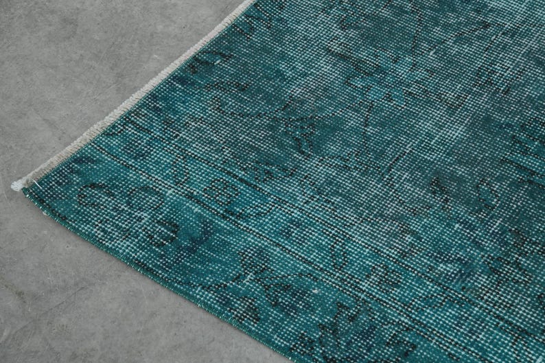 May include: Close-up of a teal blue rug with a woven texture. The rug has a distressed look with a faded pattern.