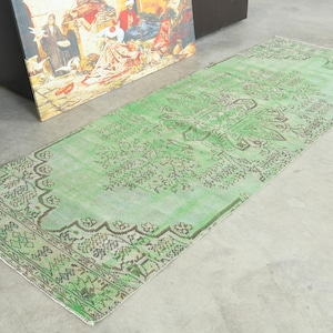 May include: A rectangular runner rug featuring a vibrant mint green base color with intricate dark brown floral and geometric patterns. The design includes a central medallion motif and a detailed border, showcasing a faded, distressed texture.