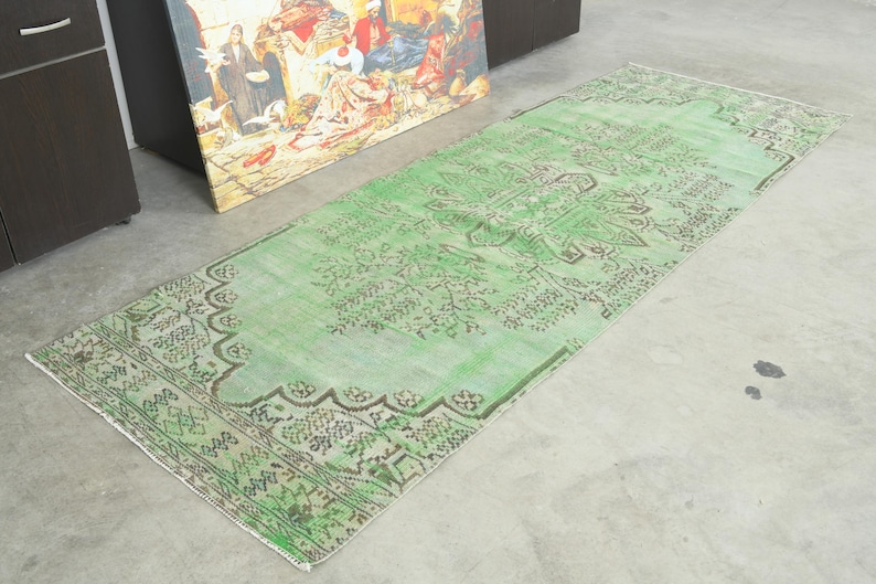 May include: A rectangular runner rug featuring a vibrant mint green base color with intricate dark brown floral and geometric patterns. The design includes a central medallion motif and a detailed border, showcasing a faded, distressed texture.