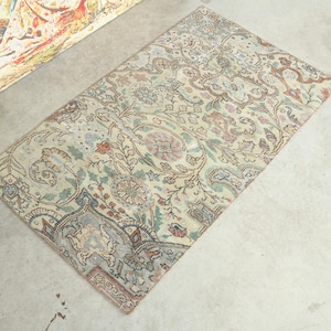 Op de afbeelding: Rechthoekig vintage tapijt met een ingewikkeld bloemmotief in crème, bruin en gedempte blauwtinten. Het tapijt heeft een centraal medaillonontwerp en een gedetailleerde rand. Het tapijt ligt op een betonnen ondergrond.