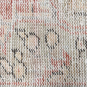 May include: Close-up of a woven rug with a textured pattern in shades of white, red, and black.