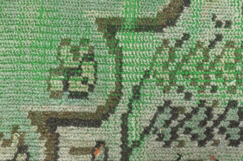 May include: A woven textile rug featuring a dense pile construction with a prominent green background. The surface displays intricate geometric and organic patterns rendered in dark brown, black, and lighter shades of green, creating a textured appearance.
