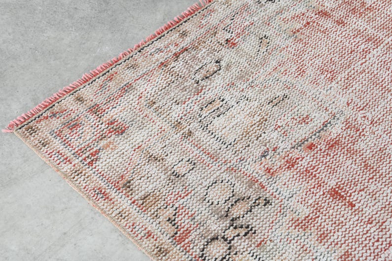 May include: A vintage rug with a cream background and a red and black geometric pattern. The rug has a fringed border.