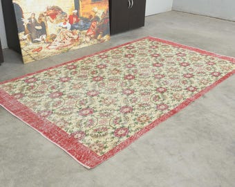 May include: A rectangular area rug featuring a cream-colored field with a repeating pattern of pink and green floral medallions. The rug is framed by a wide, solid red border that runs along all four edges of the rectangular textile piece.