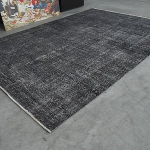 May include: A black and gray area rug with a distressed, vintage look. The rug has a subtle pattern and a white border.