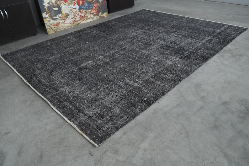May include: A black and gray area rug with a distressed, vintage look. The rug has a subtle pattern and a white border.