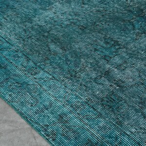 May include: A teal blue rug with a faded, distressed pattern. The rug has a woven texture and a subtle sheen.