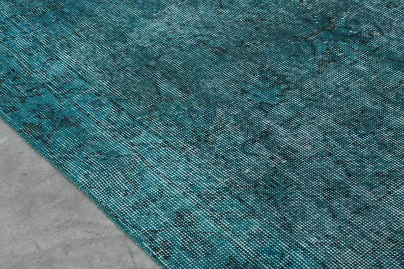 May include: A teal blue rug with a faded, distressed pattern. The rug has a woven texture and a subtle sheen.