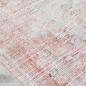 May include: A close-up of a woven rug with a cream, pink, and black colour scheme. The rug has a textured surface and a subtle pattern.