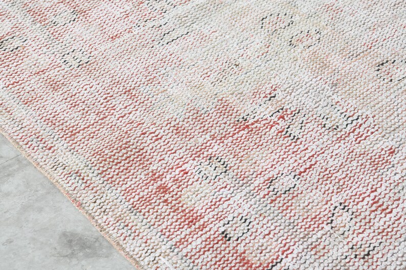 May include: A close-up of a woven rug with a cream, pink, and black colour scheme. The rug has a textured surface and a subtle pattern.