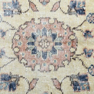 May include: A close-up of a beige rug with a detailed floral pattern in shades of blue, pink, and brown. The rug has a worn, vintage look.