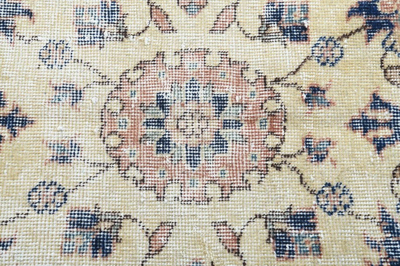 May include: A close-up of a beige rug with a detailed floral pattern in shades of blue, pink, and brown. The rug has a worn, vintage look.
